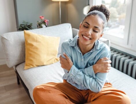 Beautiful young woman sitting on the sofa at home in the morning and hugging self